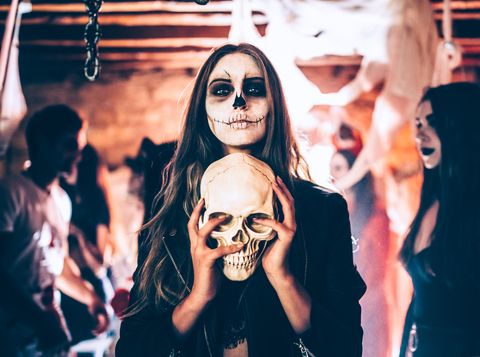 Young woman with skeleton make-up holding skull at Halloween party