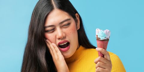 Young Woman With Toothache Holding Ice Cream Cone Against Blue Background