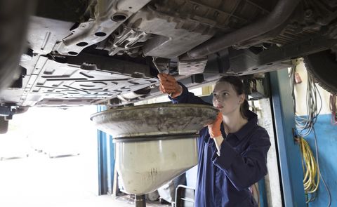 Young woman working in repair garage, changing oil