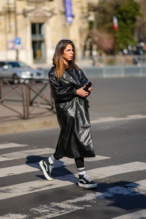 paris, france march 08 a guest wears a black hoodie sweater, a black shiny leather long coat, a black shiny leather crossbody bag from chanel, a gold love bracelet from cartier, black legging pants, black and white striped print pattern socks, black ankle sneakers from vans, outside miu miu , during paris fashion week womenswear fw 2022 2023, on march 08, 2022 in paris, france photo by edward berthelotgetty images