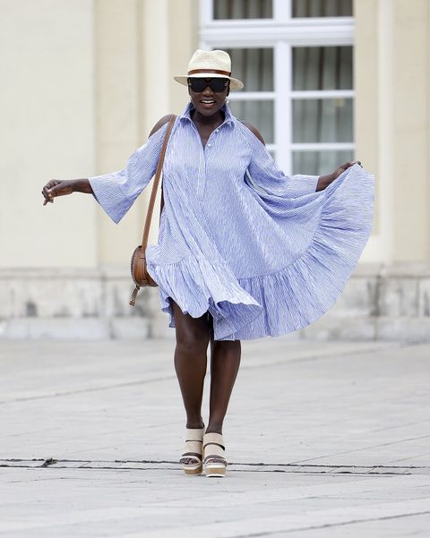 wuerzburg, germany   june 28 auma obama sister of former us president barack obama wearing a blue and white striped short cold shoulder dress with ruffle detail and shoulder cut outs by talbot runhof, a small brown bag by chloe, a vintage beige bast hat, beige wedge sandals by hogan and black oversized sunglasses by aigner during a street style shooting on june 28, 2021 in wuerzburg, germany photo by streetstyleshootersgetty images