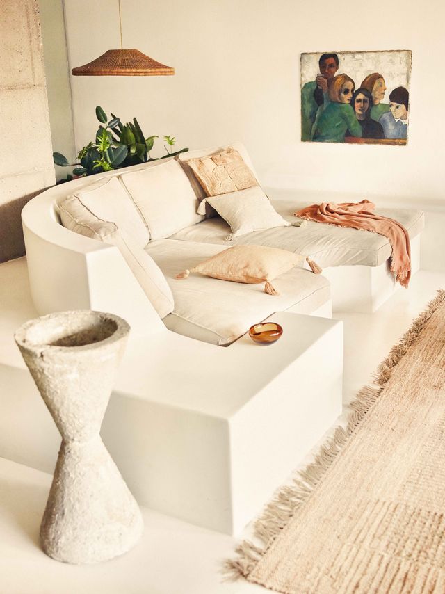 salón de estilo artesanal y mediterráneo con sofá blanco semicircular con cojines en tonos crema y lámpara de fibras artesanales