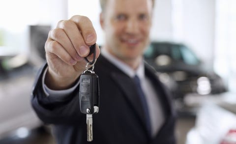 salesman holding out car key in automobile showroom