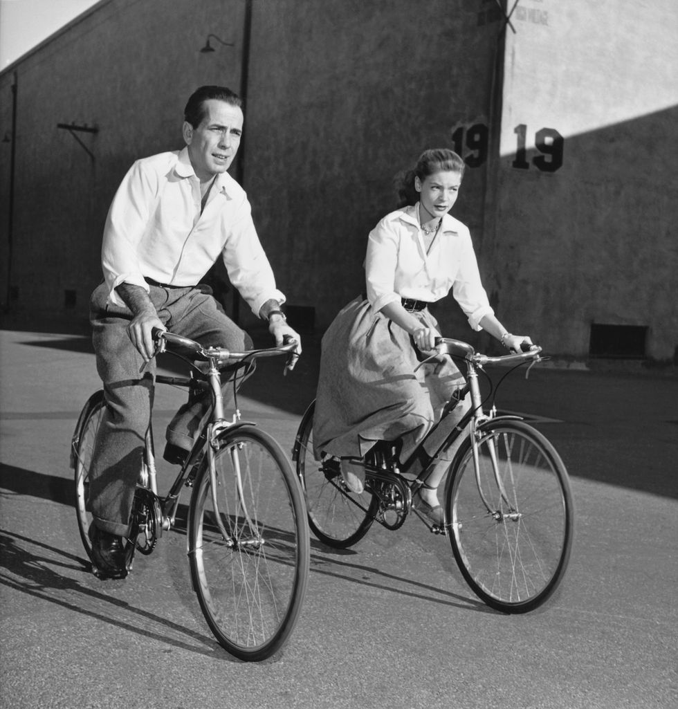Lauren Bacall and Humphrey Bogart ride bicycles while on the set of the film 'Key Largo'
