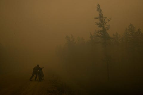 op weg naar een naburige bosbrand in de russische regio jakoeti duwt oleg sjtsjerbakov 37 lid van de plaatselijke vrijwillige brandweer zijn brommer voort door de rook