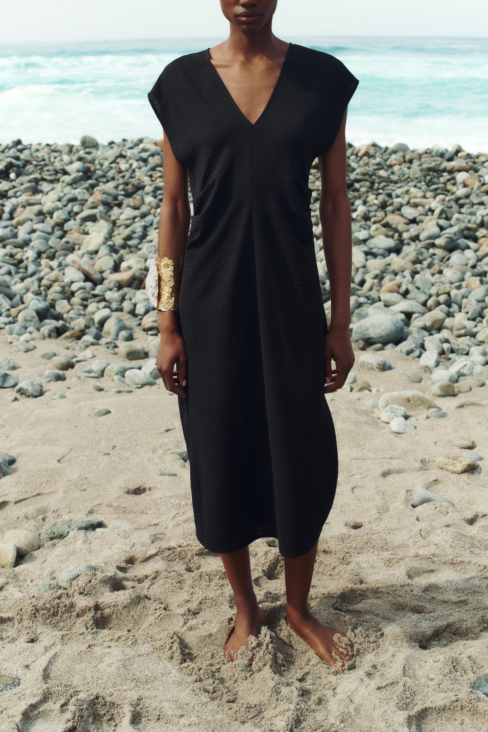 a person in a black dress on a rocky beach