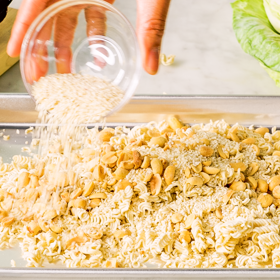 pouring sesame seeds over a mixture of ramen noodles and nuts