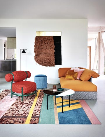 Living room with orange sofa, red chair, blue footstool, multicoloured patterned rug
