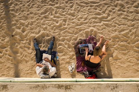 CDIZ SPANJETwee boekenwurmen baden in de Spaanse zon terwijl ze bij de zuidwestelijke havenstad Cdiz van hun favoriete leesvoer genieten