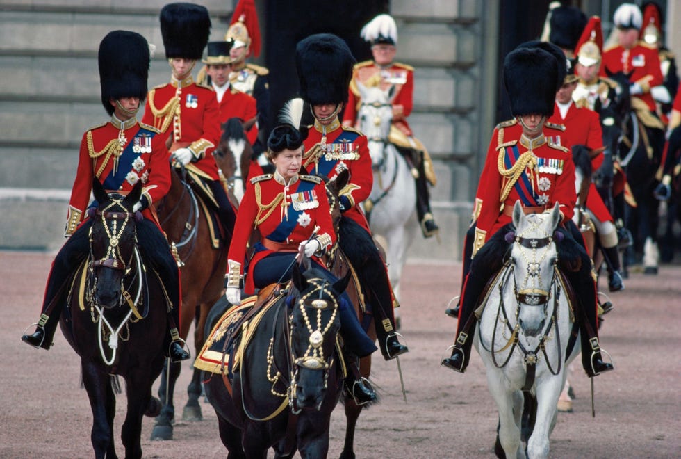 8657 In 1984 neemt Elizabeth II te paard de parade Trooping the Colour af waarbij ze wordt vergezeld van haar zoon kroonprins Charles rechts van haar en wordt gevolgd door haar man en anderen Alle deelnemers zijn gekleed in uniformen van de Welsh Guards en gedecoreerd met koninklijke medailles De mannen dragen de hoge militaire berenmuts