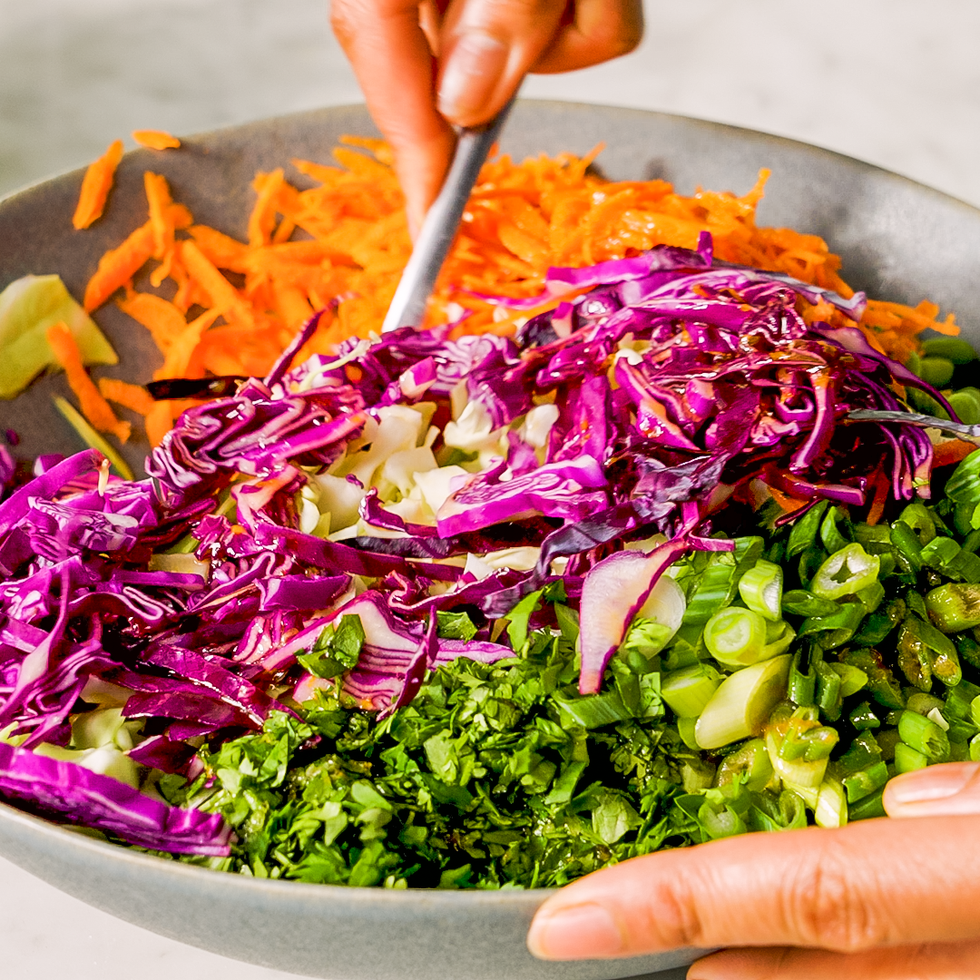 mixing thinly sliced cabbage and carrots in a bowl