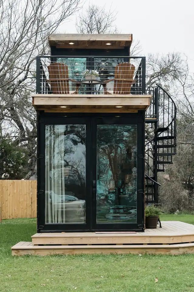 a small black structure with a glass door and a metal frame on a grass lawn with trees and