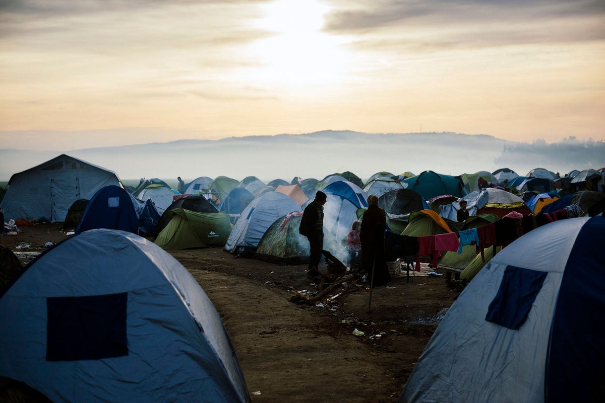 Mensen staan op 6 maart 2016 tussen tenten in een tijdelijk opvangkamp aan de GrieksMacedonische grens bij de Griekse plaats Idomeni waar duizenden migranten en vluchtelingen wachten om de grens met Macedoni over te steken