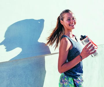 shot of beautiful female runner standing outdoors holding water bottle. fitness woman taking a break after running workout.