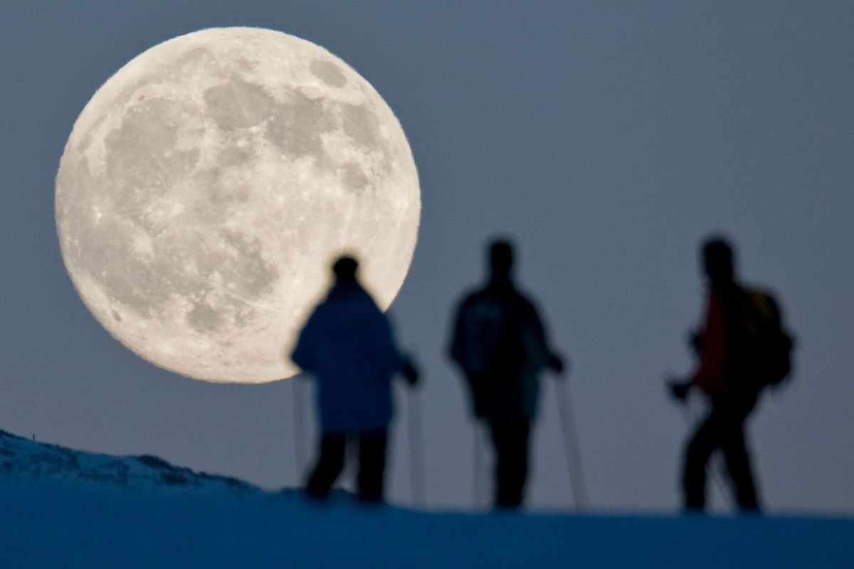 Sneeuwwandelaars kijken tijdens de winterzonnewende in 2010 naar de bijna volle maan die opkomt achter de top van de Weissfluhjoch in de Zwitserse plaats Arosa