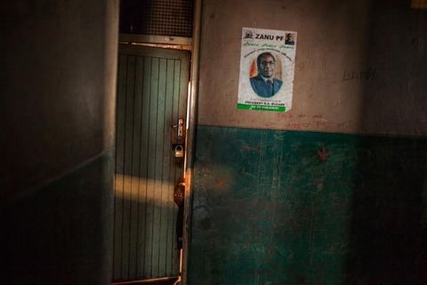 Een kind gluurt naar buiten in een hostel bij de hoofdstad Harare Op een aanplakbiljet is Robert Mugabe te zien Tijdens zijn 37jarige bewind ging het land ten gronde en sloegen miljoenen mensen op de vlucht