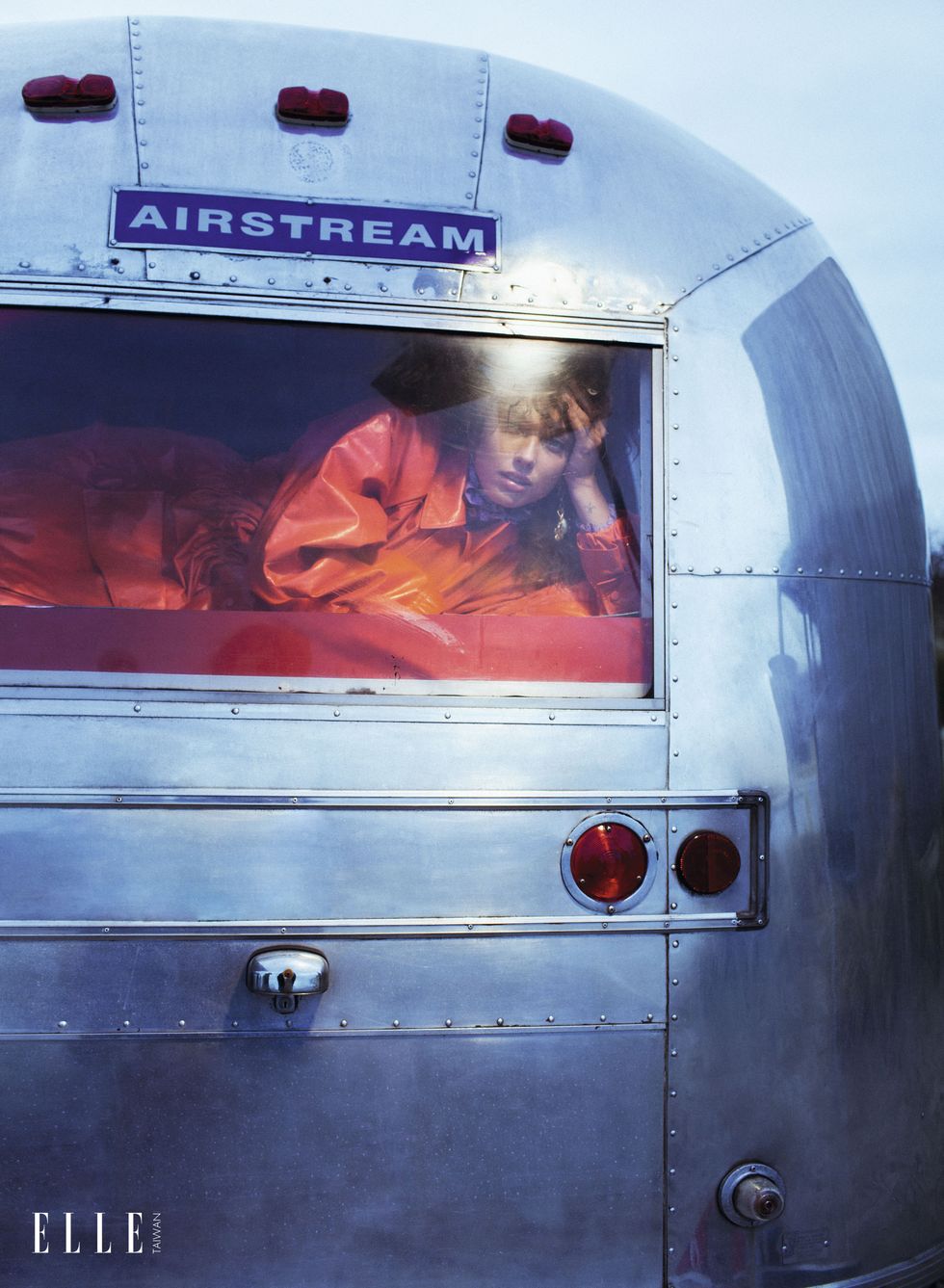 一個女人穿著橘色漆皮風衣臥在麵包車中