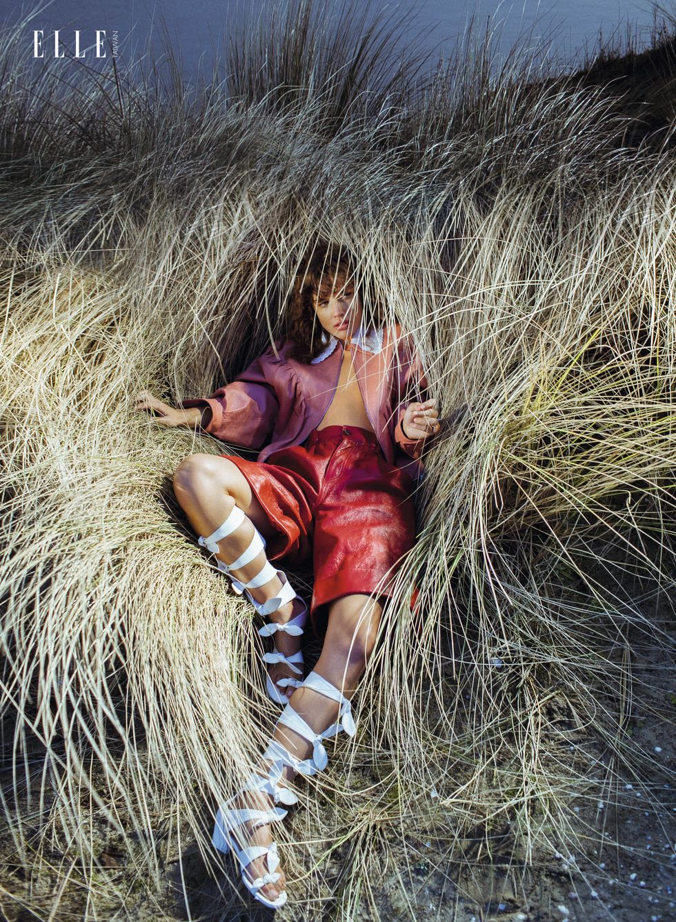 一個女人穿著皮革外套、皮革短褲臥在乾草堆中