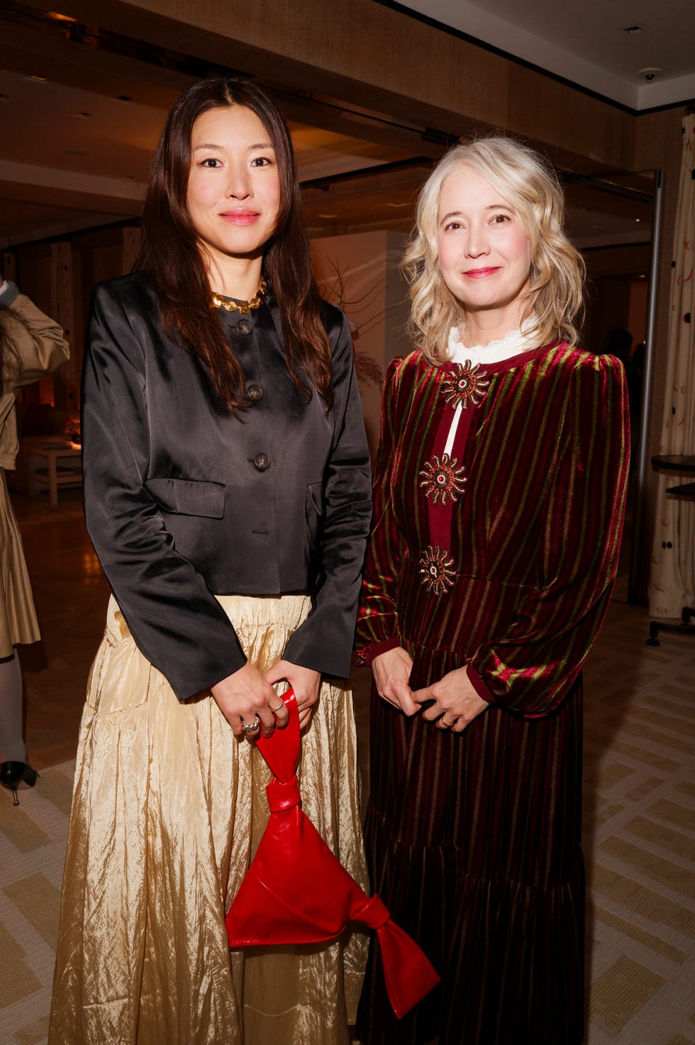 two women dressed in stylish outfits one holding a small red bag