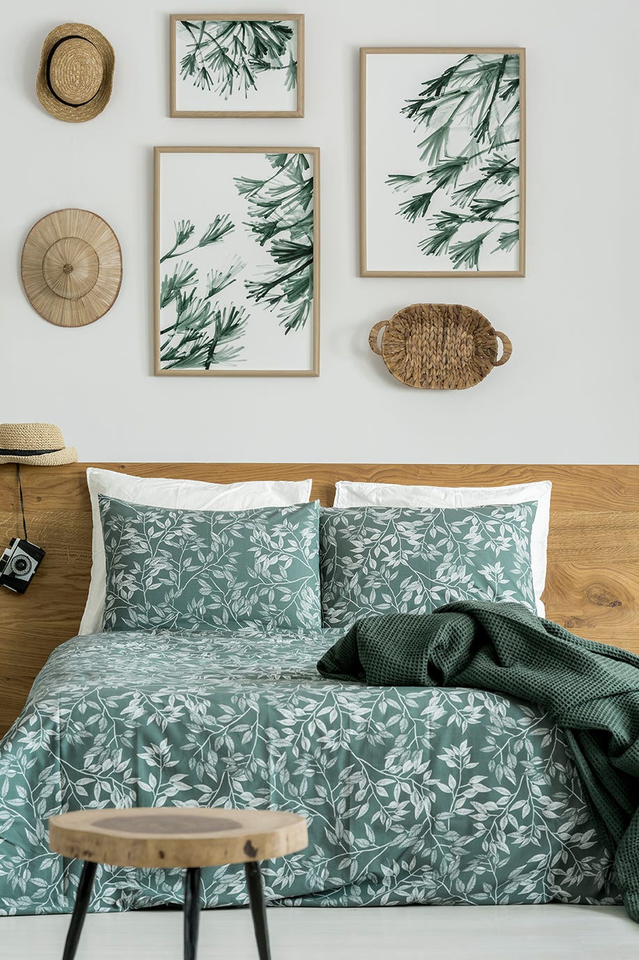 green patterned bedsheets and pillows on king size bed against wall with souvenirs and paintings of leaves in traveler's bedroom