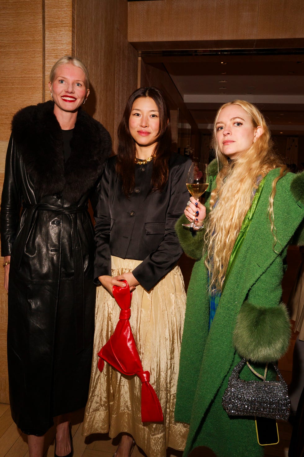 three women dressed in stylish outfits each holding accessories pose together