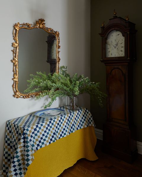 entry table with base yellow draping and a blue and gold check overlay fabric and a gilded mirror above it and a grandfather clock in the corner