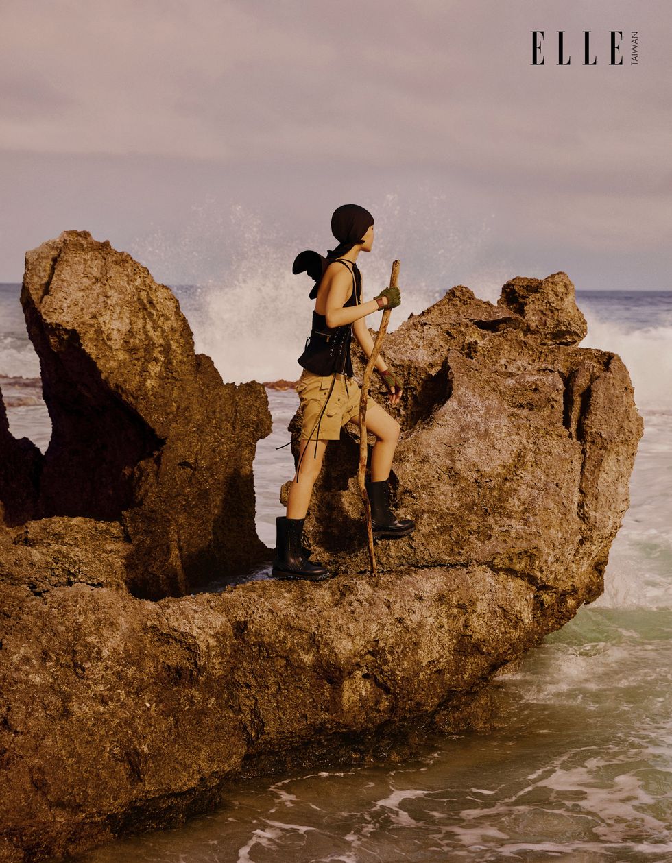 一個女人穿著背心短褲站在礁岩上
