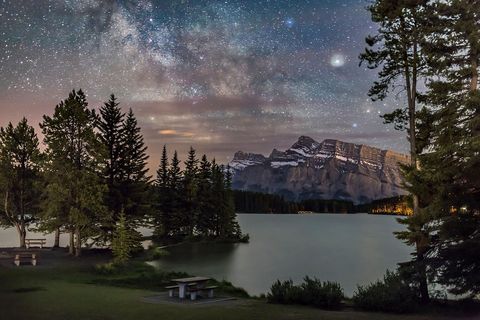 Boven Banff in Alberta Canada glanst een crmekleurige Saturnus in juni 2016 helder aan de rechterzijde van de Melkweg