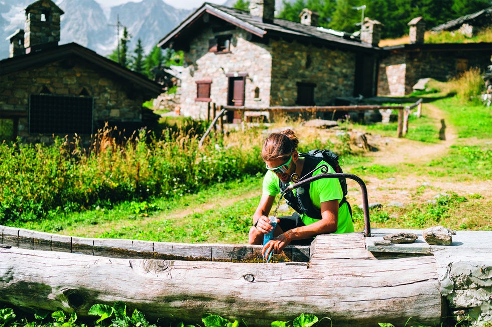 trail runner pauses in mountain field to fill water bottle from fountain