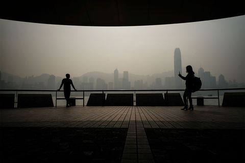 Toeristen nemen fotos op de promenade van Kowloon terwijl een dikke laag smog de beroemde skyline van Hongkong bedekt
