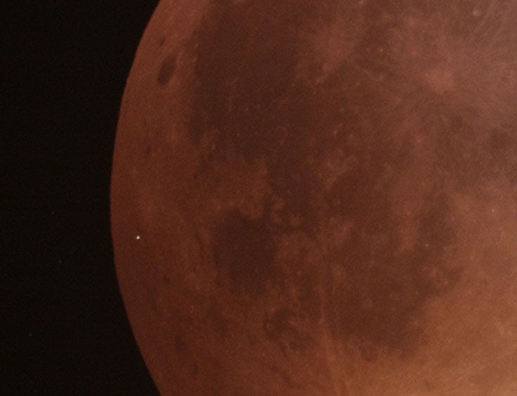 Op een closeup van het donkere oppervlak van de bloedmaan is de flits van de meteoorinslag te zien