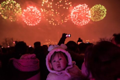 Het herdenkingsvuurwerk werpt een roze schijnsel over het gezicht van een baby De zogenaamde Dag van de Schijnende Ster wordt ook vijf jaar na de dood van Kim Jong Il nog altijd met grootse festiviteiten gevierd