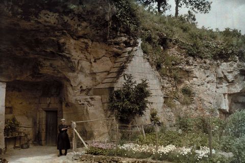 Een vrouw staat voor een grotkerk in het dorpje Courtineau Frankrijk