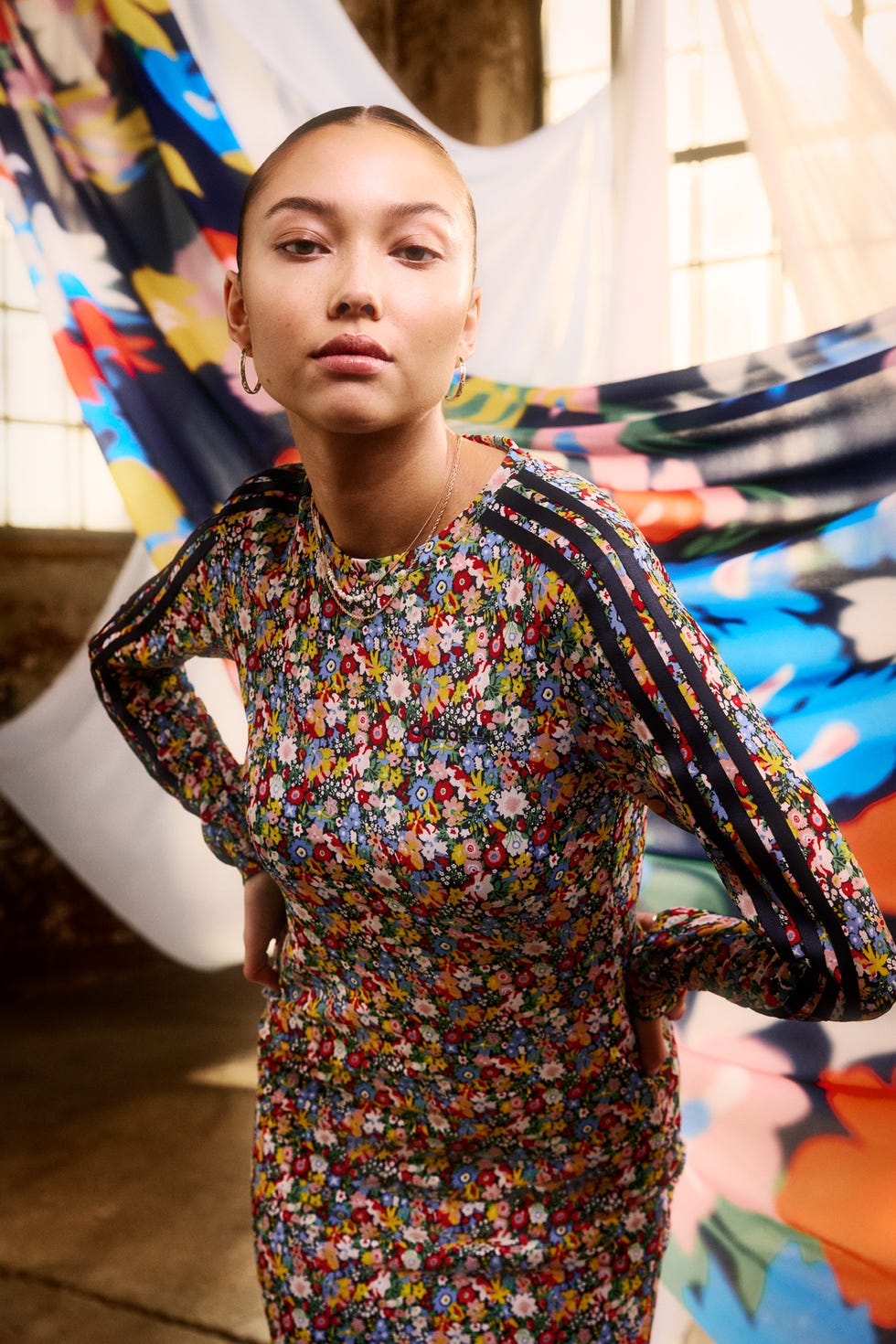 a person dressed in a colorful floralpatterned outfit poses in front of vibrant fabric drapes