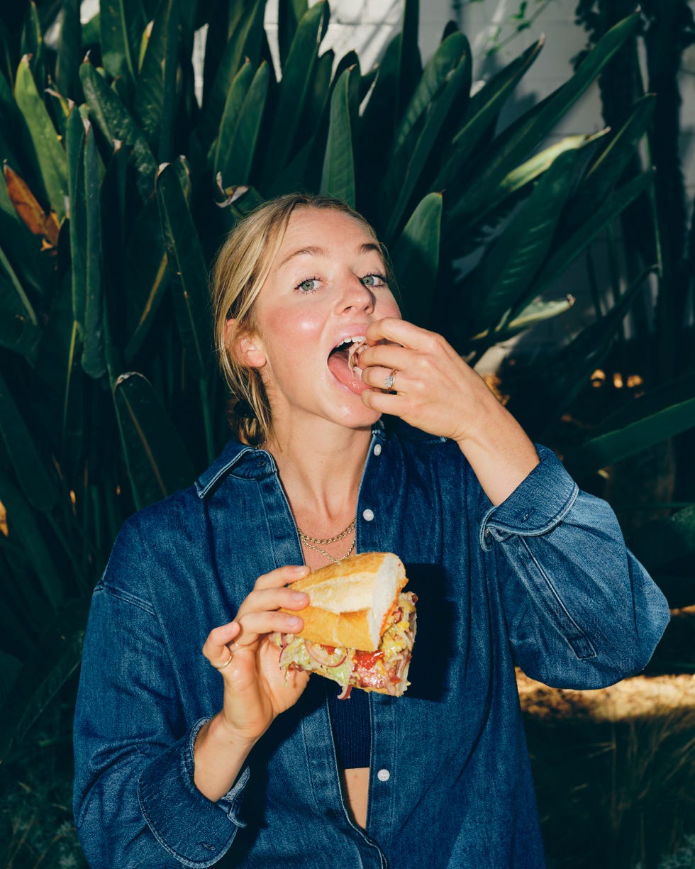 person holding a large sandwich in front of green foliage