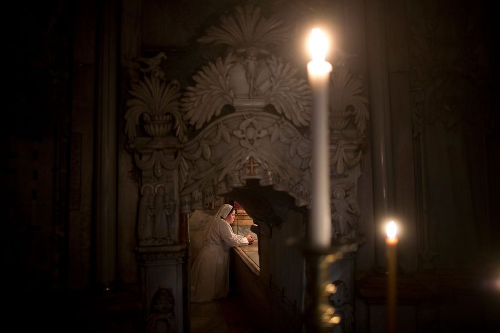 In de grafschrijn of Aedicula knielt een christelijke non in gebed voor het grafbed van Christus
