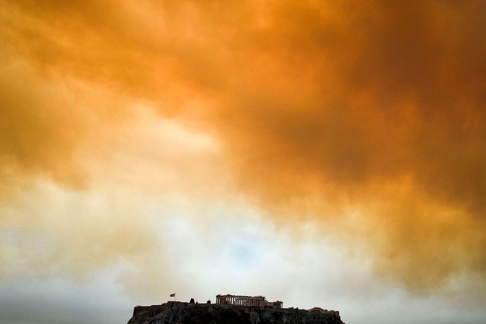 Achter het Parthenon de oude Griekse tempel op de Akropolis in Athene zijn in de verte de donkere rookwolken van de natuurbrand in het naburige plaatsje Kineta te zien