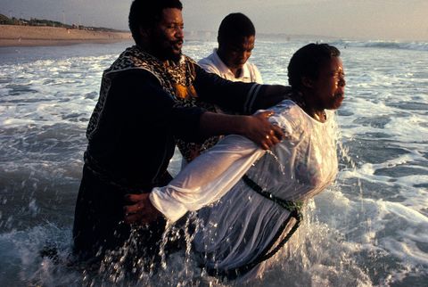 Bij Durban in ZuidAfrika wordt een lid van de Church of Zion in de Indische Oceaan gedoopt