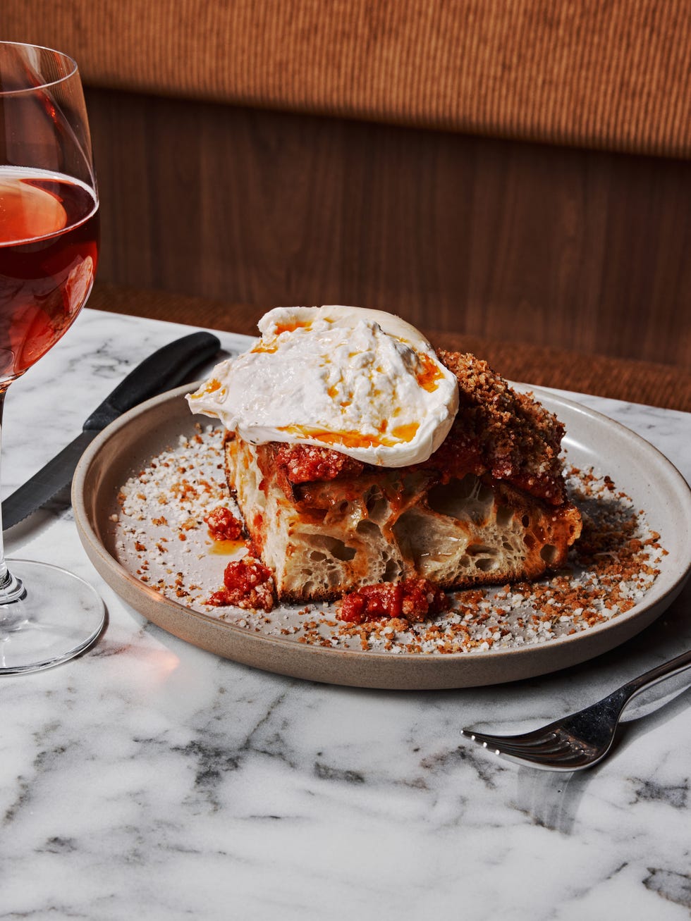 a plate with a slice of bread topped with sauce and a poached egg accompanied by a glass of red beverage