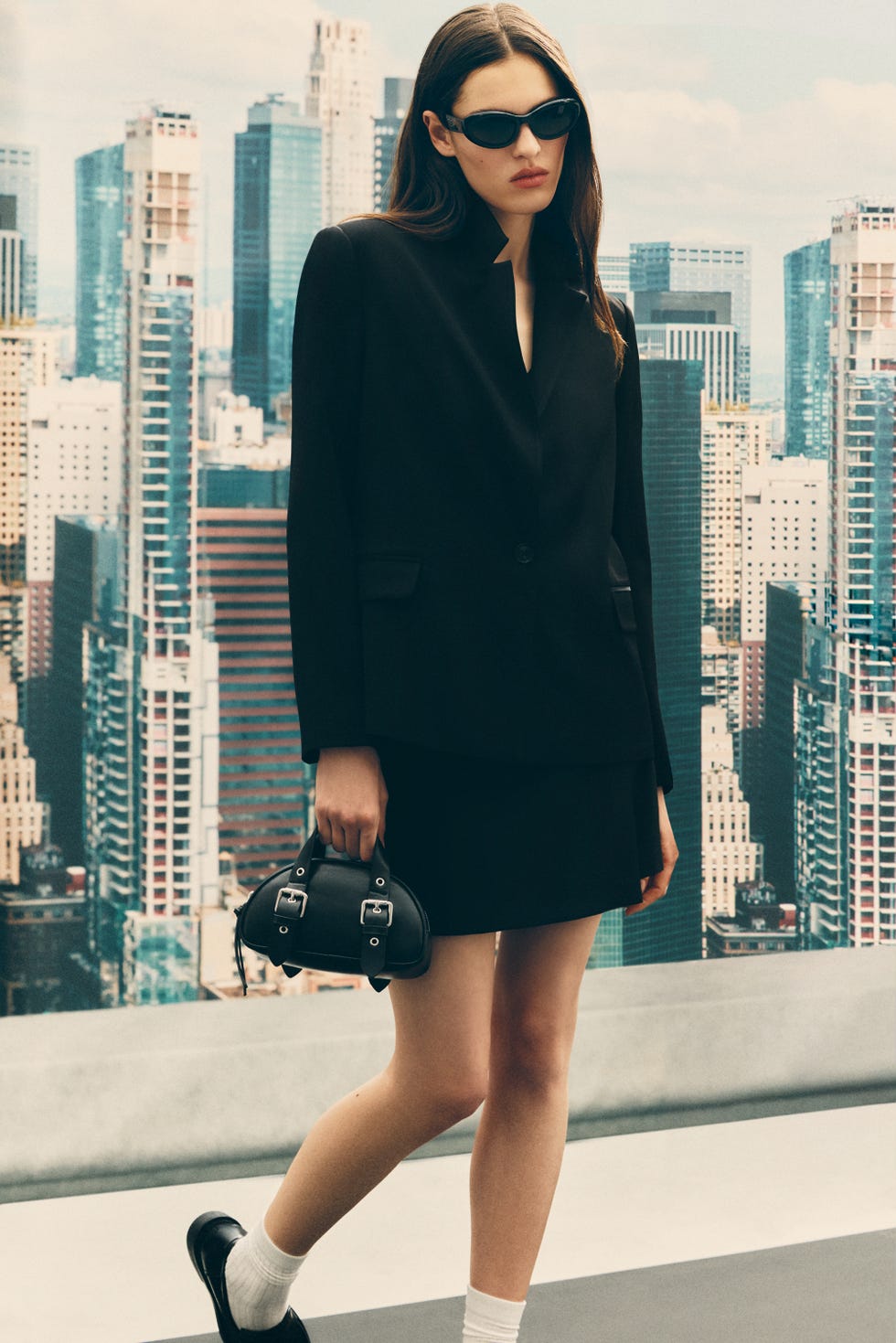 a model showcases a chic black outfit against a city skyline backdrop