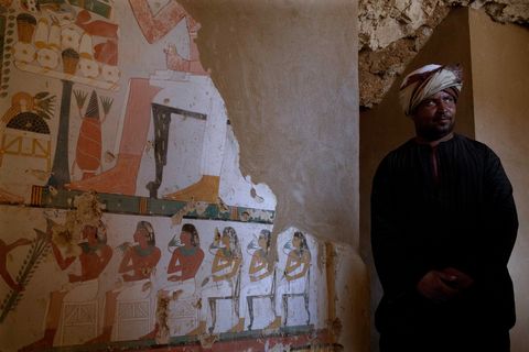 Een medewerker staat naast een weelderige grafschildering op de wand van de pas ontdekte tombe in de Egyptische necropolis Dra Abu elNaga