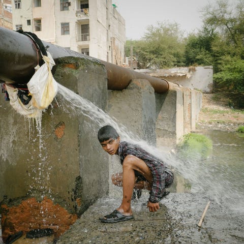 Een jongen spoelt zich af nabij een riool waar hij heeft gezocht naar afvalmateriaal dat hij kan verkopen aan recyclingbedrijfjes