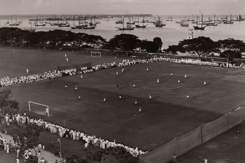 Toeschouwers omringen een voetbalveld bij de haven van een eiland in de Stille Oceaan De sport werd meegebracht door de eerste Europeanen die deze eilanden koloniseerden