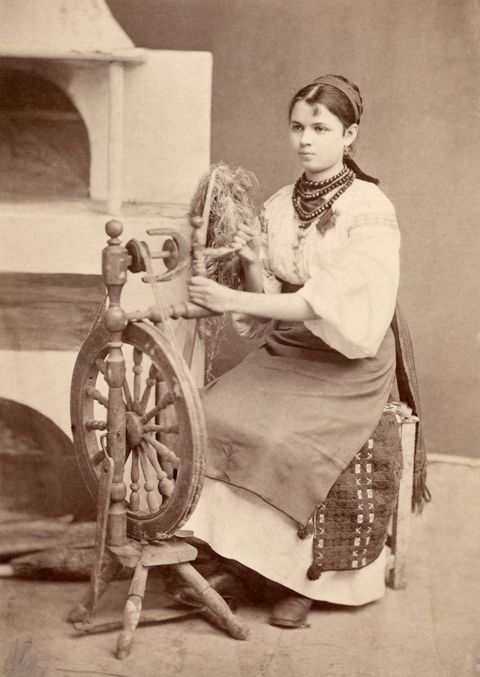 Een Oekraense vrouw in traditionele klederdracht werkt aan een spinnenwiel 1918