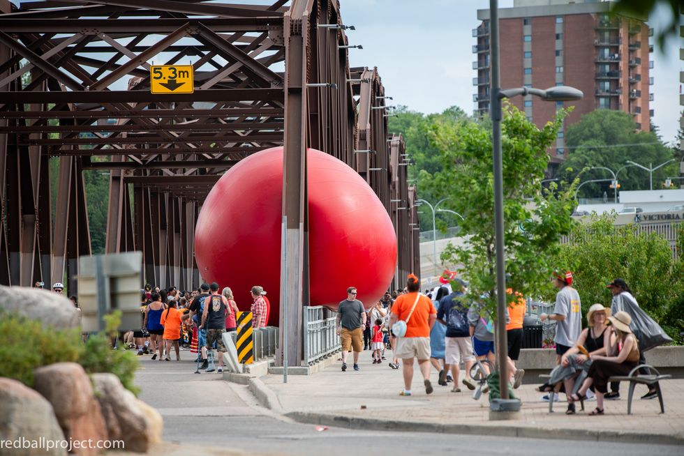 a group of people walking on a sidewalk next to a large red balloon