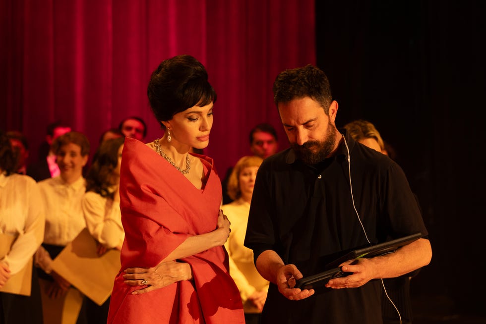 A woman in an elegant outfit converses with a man holding a device on a stage