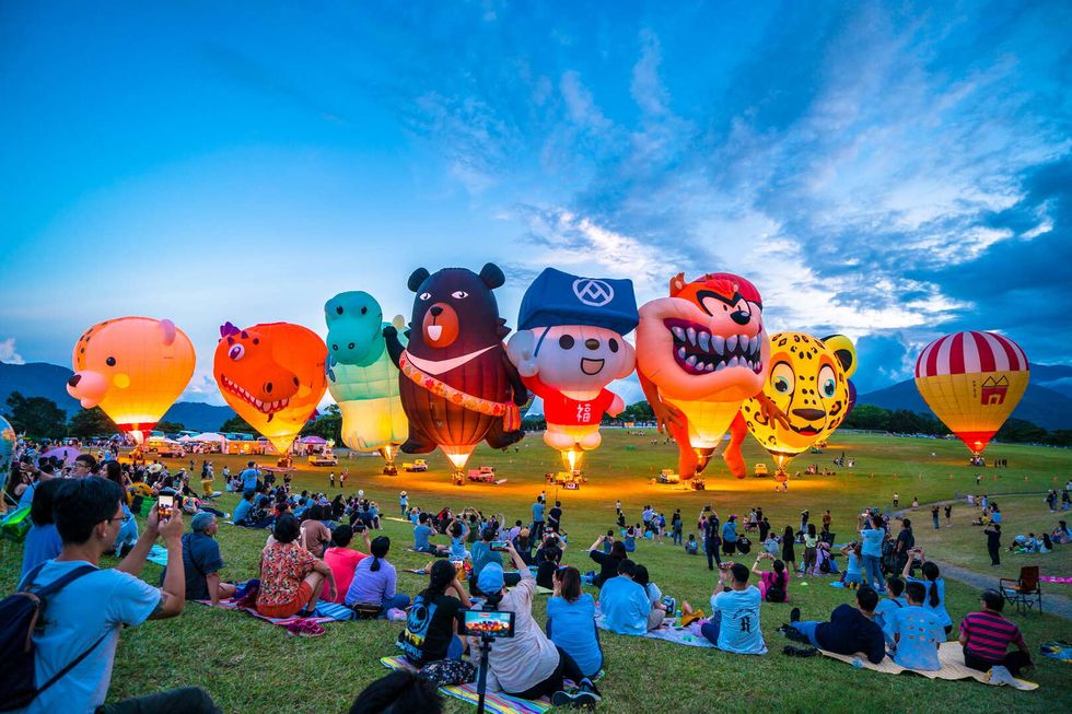 a group of people sitting on grass with hot air balloons in the air