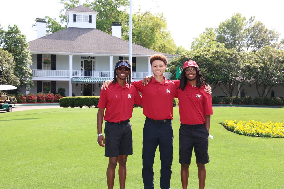 Three individuals standing together in a green outdoor area with a building in the background.