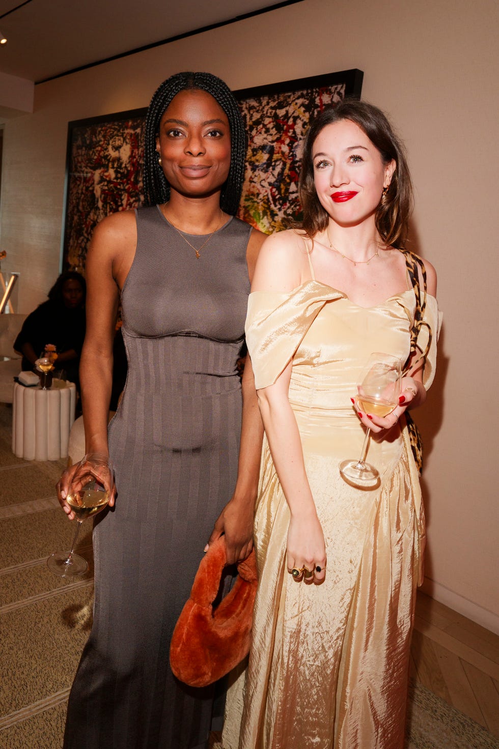 two women dressed in evening attire holding drinks at a social gathering