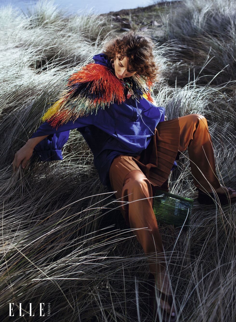 一個女人穿著風衣、彩色草編披風臥在草堆中